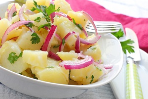 Kartoffelsalat mit roten Zwiebelstreifen und frischer, glatter Petersilie, angerichtet in einer weißen Schale